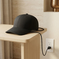 The Luxuel Laser Cap 272 on a side table with its cable running to a wall outlet — the device is mains-powered and used while plugged in