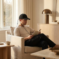 A man reading in an armchair wearing the Luxuel Laser Cap 132, its power cable running from the cap