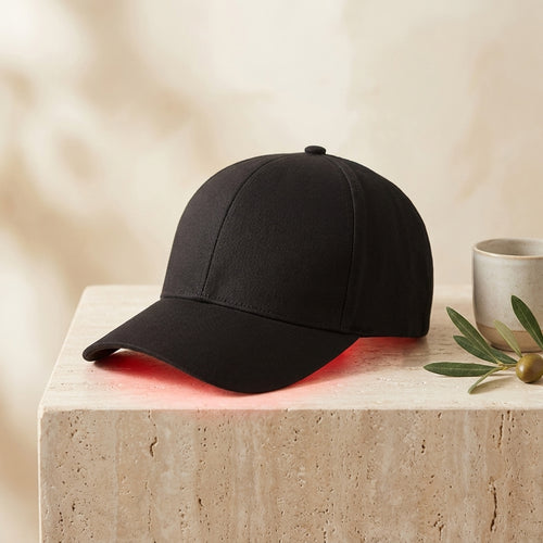 Luxuel Laser Cap 128 black laser hair growth cap on a travertine pedestal